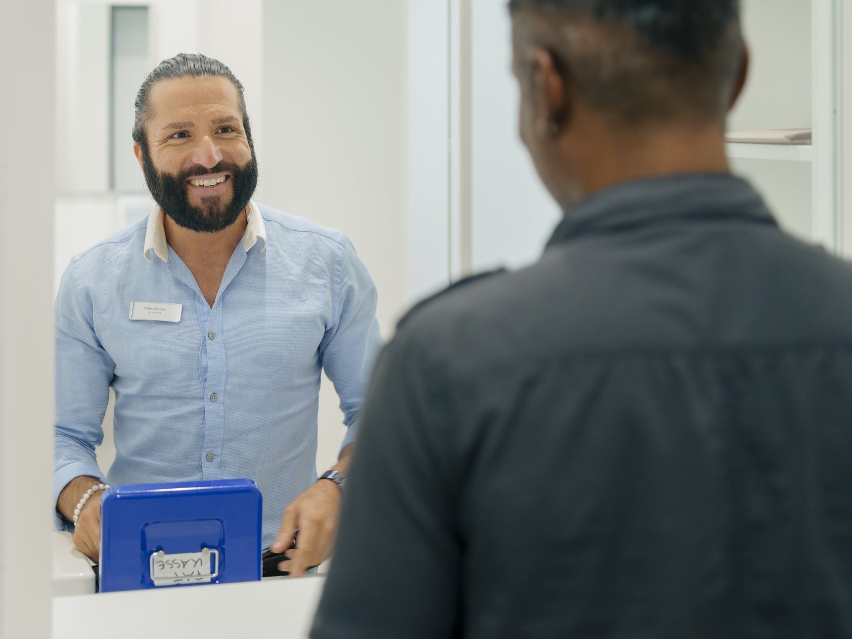 Ein Mann arbeitet an der Kasse und laechelt seinen Kunden an