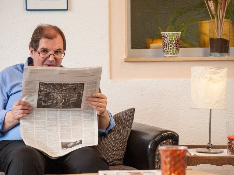 Ein Mann mit Brille sitzt in einem Ledersessel und liest Zeitung