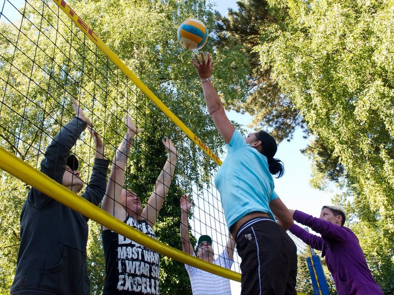 Action: eine Gruppe Frauen und Männer spielen Volleyball - eine Frau "lupft" gerade den Ball über den "Block"